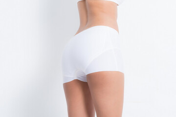 Detailed shot focusing on a woman's hip and leg area in white underwear concepts beauty and health studio on white background.