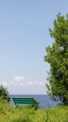 A bright green wooden bench sits on a grassy hilltop, offering a peaceful view of the lake and...