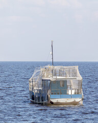 Rear view of a blue fishing boat anchored in calm waters, fully wrapped in protective netting under...