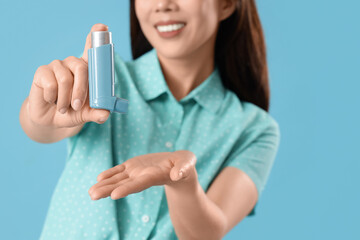 Happy young woman with inhaler on blue background, closeup