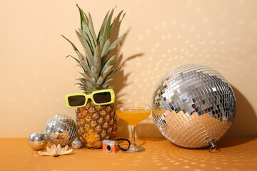 Disco balls with pineapple, cocktail and beach decor on color background