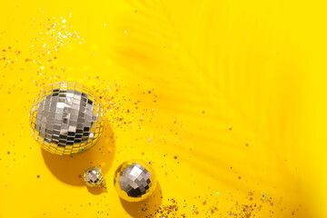 Disco balls with confetti and palm leaf shadow on yellow background