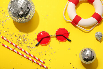 Disco balls with sunglasses, straws and lifebuoy on yellow background