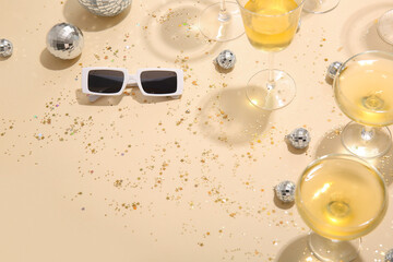 Disco balls with glasses of champagne, sunglasses and confetti on beige background