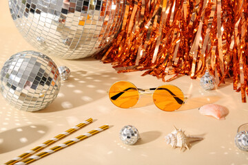 Disco balls with tinsel, seashells and sunglasses on beige background