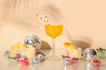 Cocktail with disco balls, ice and fruits on beige background