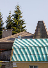 Close-up view of various rooftops in a rural area, featuring green corrugated metal and brown tiled...