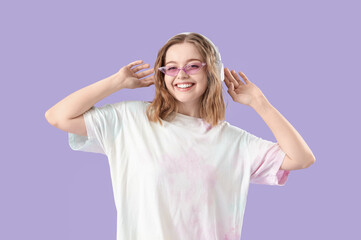 Cool young woman listening to music and dancing on lilac background