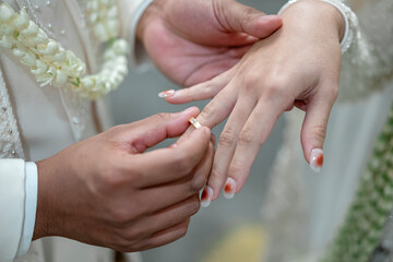 Groom placing a wedding ring on the bride's finger during a traditional Indonesian wedding...