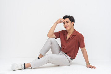 A relaxed young Asian man smiling confidently, seated on the floor with one hand propping him up...