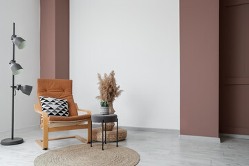 Comfortable armchair, floor lamp and vase with pampas grass near white wall in interior of living...