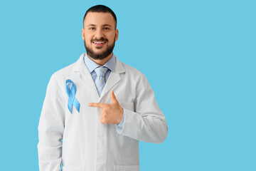 Male doctor pointing at blue ribbon on color background. Prostate cancer awareness concept