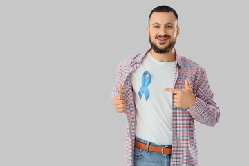 Young man pointing at blue ribbon on light background. Prostate cancer awareness concept