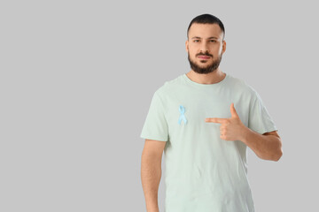 Young man with blue ribbon on light background. Prostate cancer awareness concept