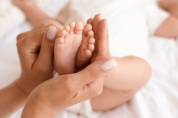 Female hands holding little baby's feet on bed, closeup