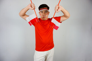Portrait a proud Indonesian man wearing red with flag face paint and headband holds and waves two...