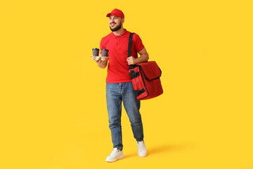 Male worker of food delivery service with bag and coffee cups on yellow background