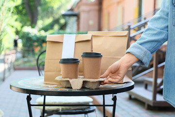 Woman with paper bags and coffee cups on table in outdoor cafe. Food delivery service