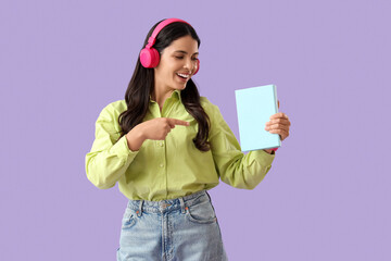 Naklejka premium Beautiful woman in headphones pointing at book on lilac background