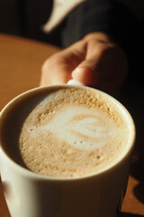 A hand holds a cup of latte with intricate foam art on top