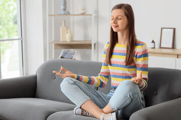 Young woman meditating on sofa at home