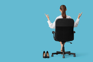 Young businesswoman with high heels meditating in chair on blue background, back view