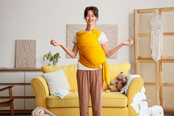 Young woman with baby in sling meditating at home