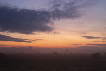 A misty dawn in a field with bales of hay