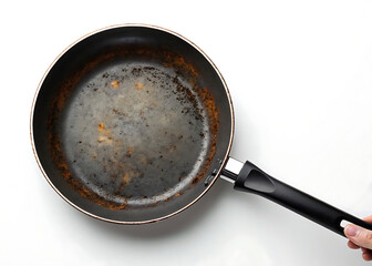 Overhead shot of a used and dirty non stick frying pan with a black handle on a white background