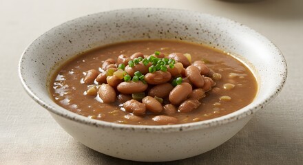 A speckled bowl filled with pinto bean soup and garnished with green chives on a neutral background