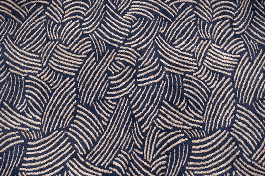 Abstract seamless pattern of a dark blue and beige carpet texture. Top-down view of woven fabric with curved lines, suitable as a background.