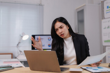 Stressed asian businesswoman having problems with laptop and documents at office desk