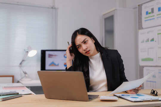 Stressed asian businesswoman having problems at work while analyzing charts on laptop and documents