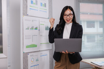 Excited businesswoman celebrating success with laptop and charts