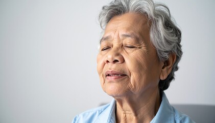 Obraz premium An older woman with elegant gray hair styled in soft waves, wearing a vibrant blue shirt, smiles warmly against a bright, natural background.