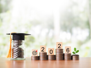Glass bottle with graduation hat and plant growing up on stack of coins. The concept of saving money for education, student loan, scholarship, tuition fees in year 2026