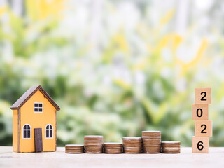 Miniature house, Wooden blocks with number 2026 and stack of coins. The concept of saving money for house, Property investment, House mortgage, Real estate in year 2026.