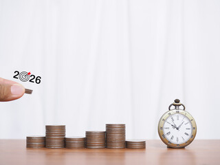 Hand putting coin into stack of coins and vintage watch. The concept of business growth, Financial investment, Market stock, Profit return, Dividend and Business fund in year 2026