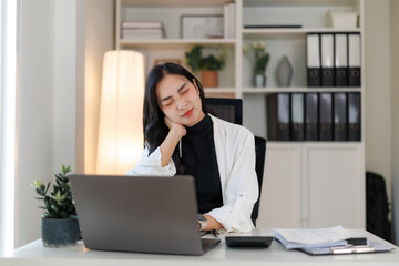 Tired asian businesswoman suffering from neck pain while working on laptop in office