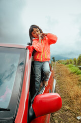 Asian little girl peeking out from car window, smiling and showing love sign with her hands, enjoying her road trip adventure to the mountain