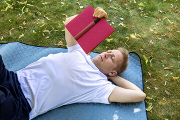 man lying on back reading book on blanket outdoors