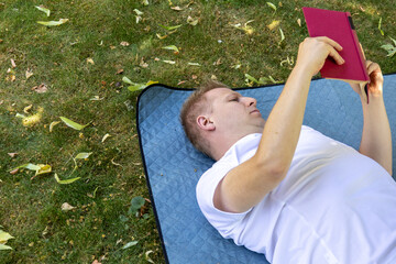 man lying on back reading book on blanket outdoors