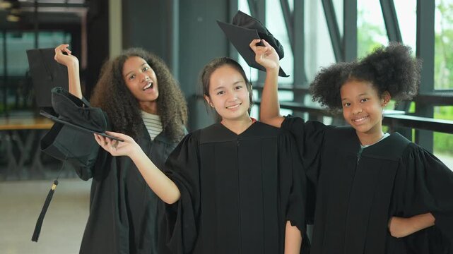 Girls of diverse ethnicities including Asian, White , African American&mdash;celebrate their graduation together in scool, wearing caps and gowns, smiling brightly as they share this proud and happy milesto