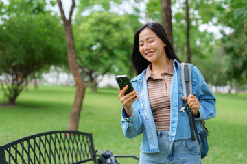 Smiling student using smartphone in park near bench