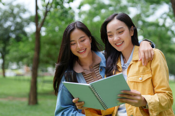 Two happy students reading a book, enjoying time together in the park