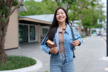 Smiling student walking on campus holding book and backpack