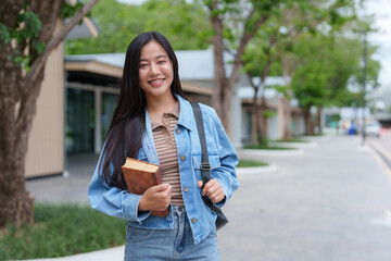Smiling student walking on campus holding book and backpack