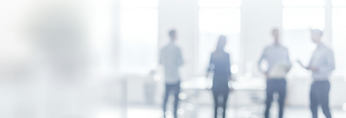 Blurred group of people standing in a bright office space.