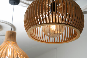 Close up of glowing light bulb inside modern wooden pendant lamp with stylish slatted design and...