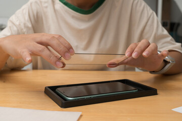 Hands placing tempered glass screen protector onto smartphone during installation process on wooden surface